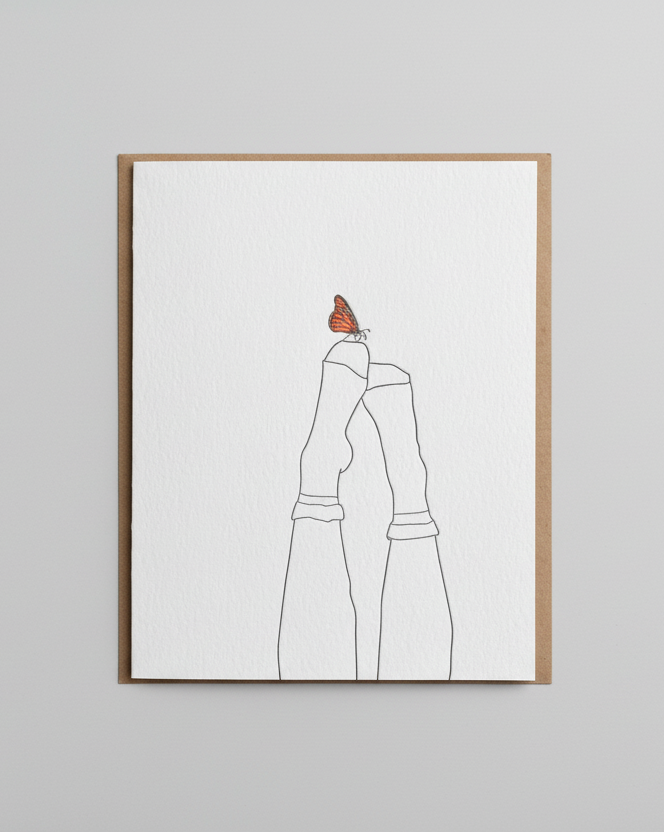 Note card with a line drawing of a person wearing a dress and a butterfly on their shoulder, placed on a wooden surface.