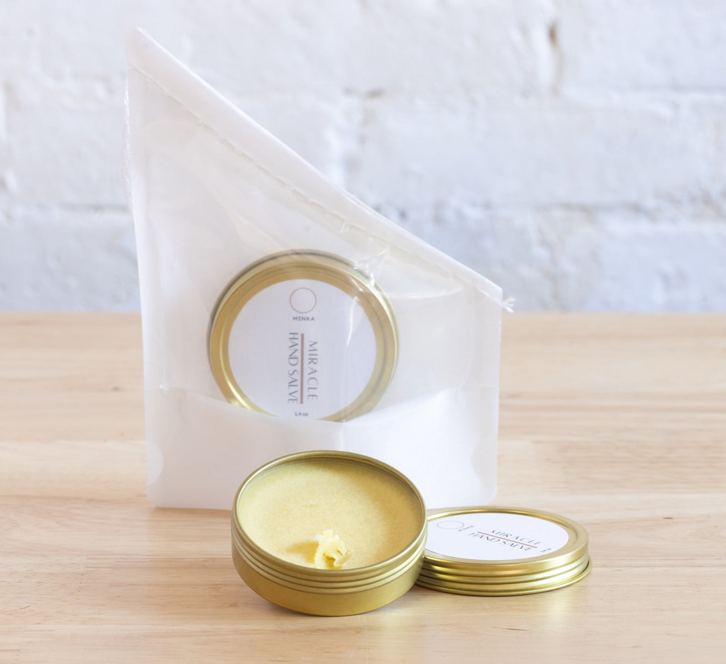A small open tin of hand salve with a solid white color and a label that reads 'Miracle Hand Salve'. The product is placed on a wooden surface with a white backdrop.