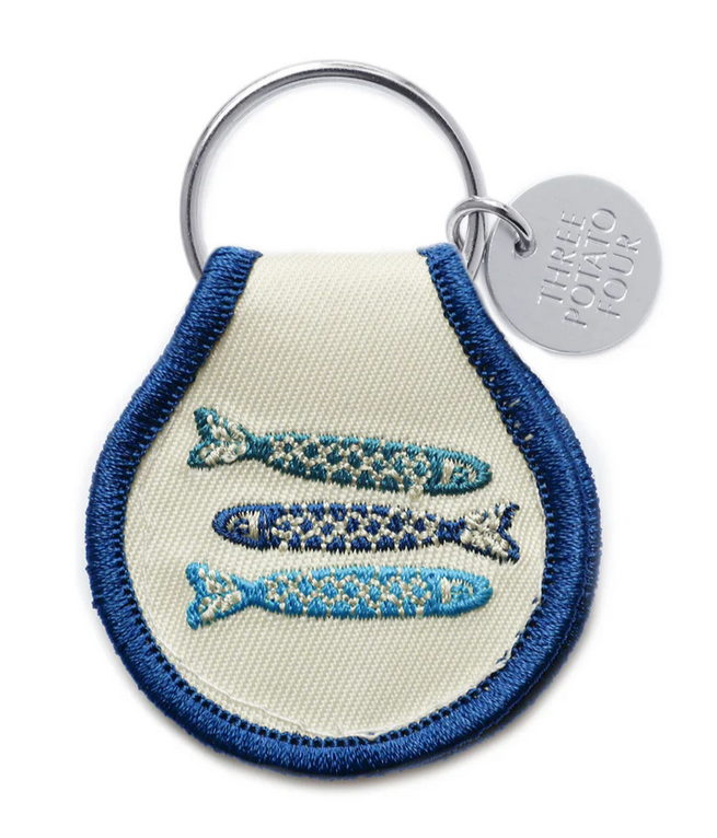 A beige keychain with blue and green embroidered fish on a split metal ring.