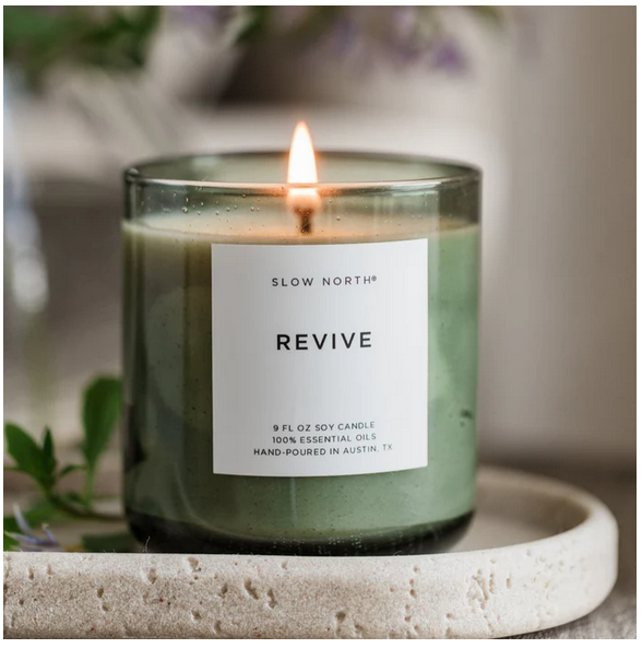 Candle labeled 'Revive' by Slow North on a stone surface with a blurred background