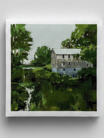 Framed cross-stitch art of a house by a lake on a gray background