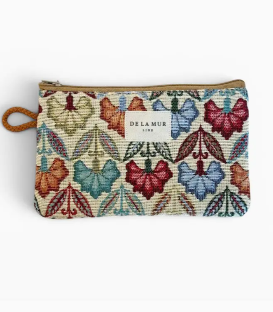 A zippered pouch featuring a colorful embroidered butterfly and leaf pattern on a cream background, with a tan zipper and a small white Delamur Line label.
