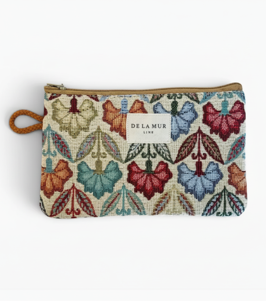 A zippered pouch featuring a colorful embroidered butterfly and leaf pattern on a cream background, with a tan zipper and a small white Delamur Line label.