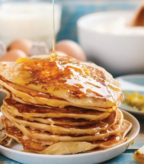 Stack of pancakes with syrup being poured over them on a white plate.