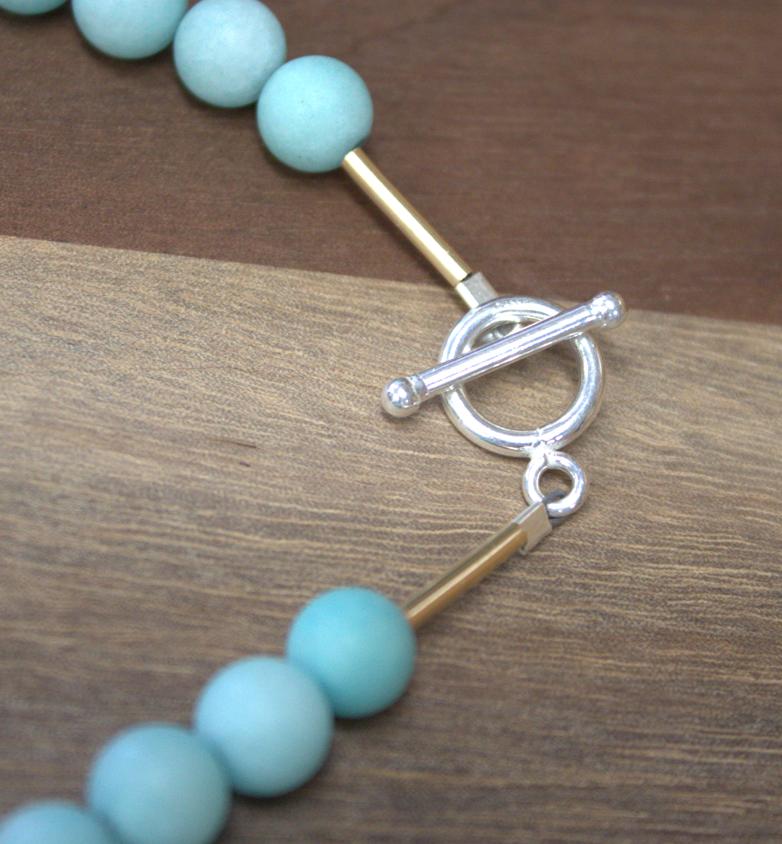 Turquoise beaded necklace with a silver clasp on a wooden surface