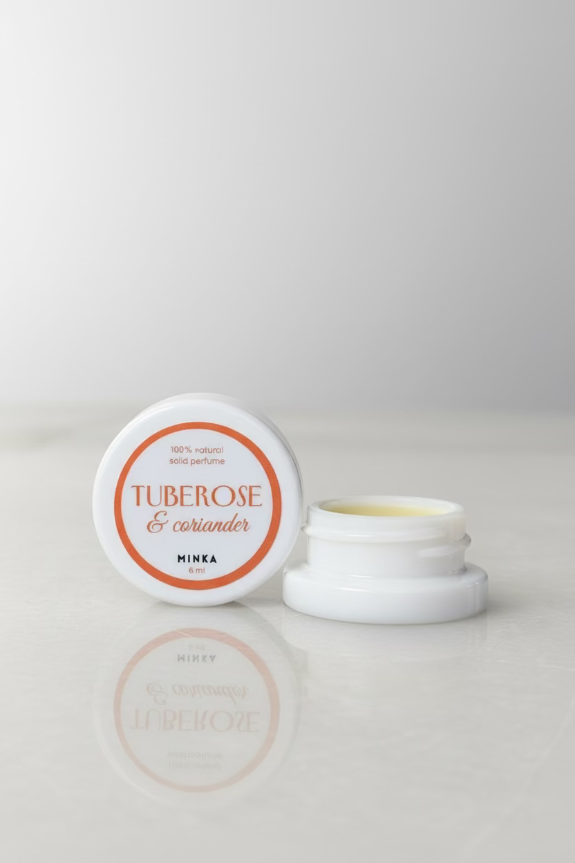 Small container of tuberose and coriander body butter on a reflective surface with a blurred background