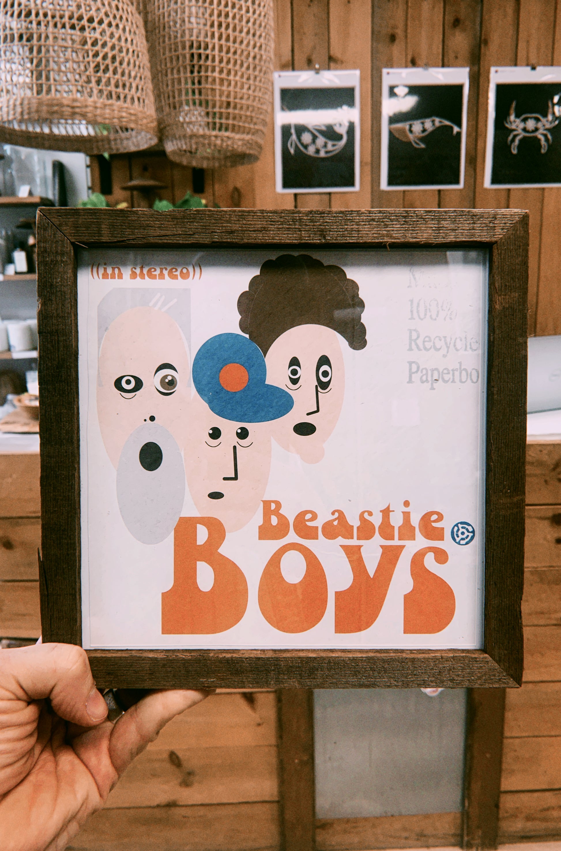 Framed poster of Beastie Boys with wooden frame held by a hand against a wooden wall background.