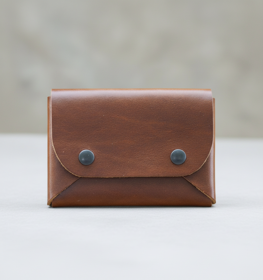 Brown leather wallet with metal buttons on a wooden surface with rocks