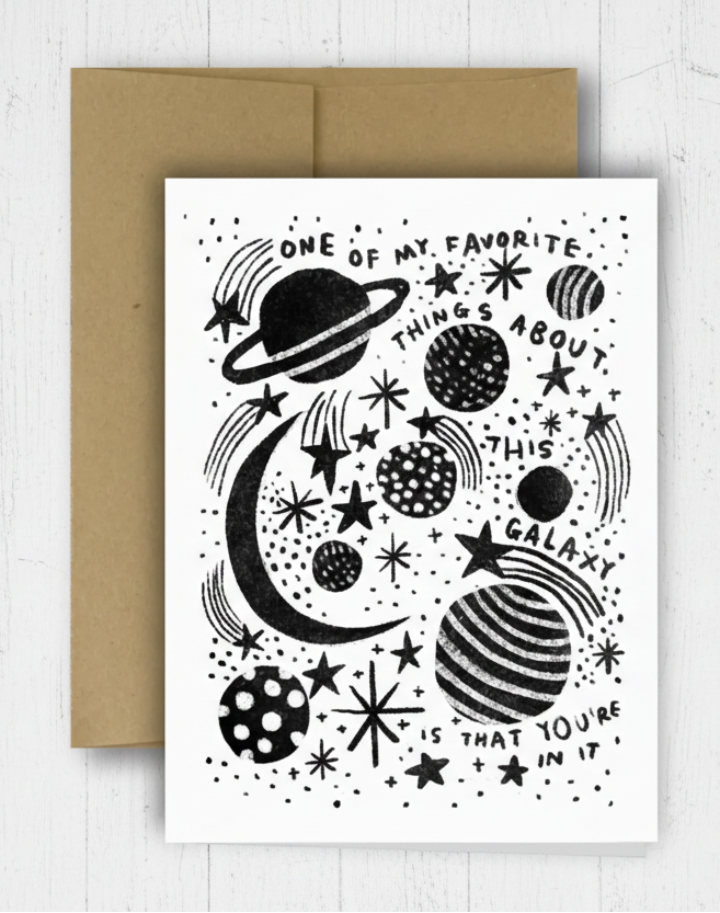 Greeting card with space-themed design and brown envelope on a checkered background