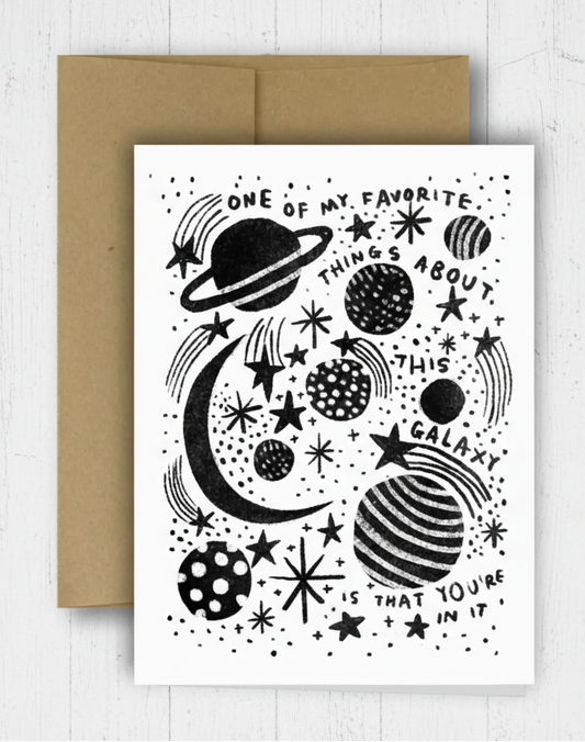 Greeting card with space-themed design and brown envelope on a checkered background