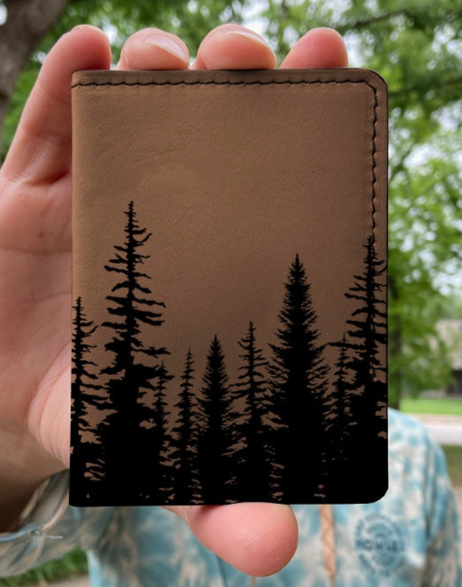 Brown leather wallet with black tree design held by a person outdoors