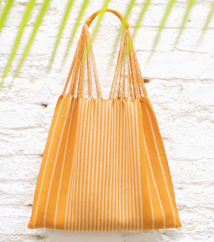Yellow striped bag on a light wooden surface with green leaves in the background