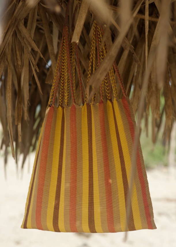 Striped bag with red and yellow pattern hanging under a thatched roof