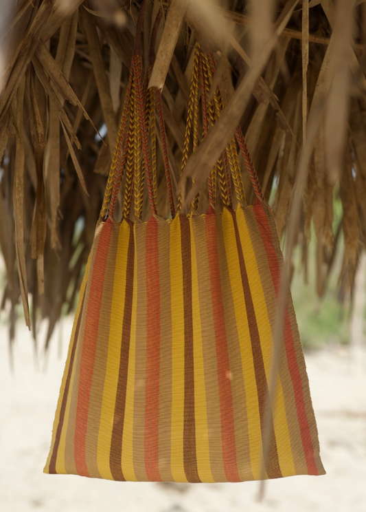Striped bag with red and yellow pattern hanging under a thatched roof