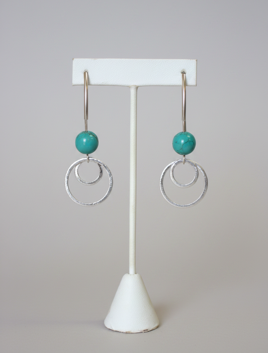Silver earrings with turquoise beads on a white stand against a plain background
