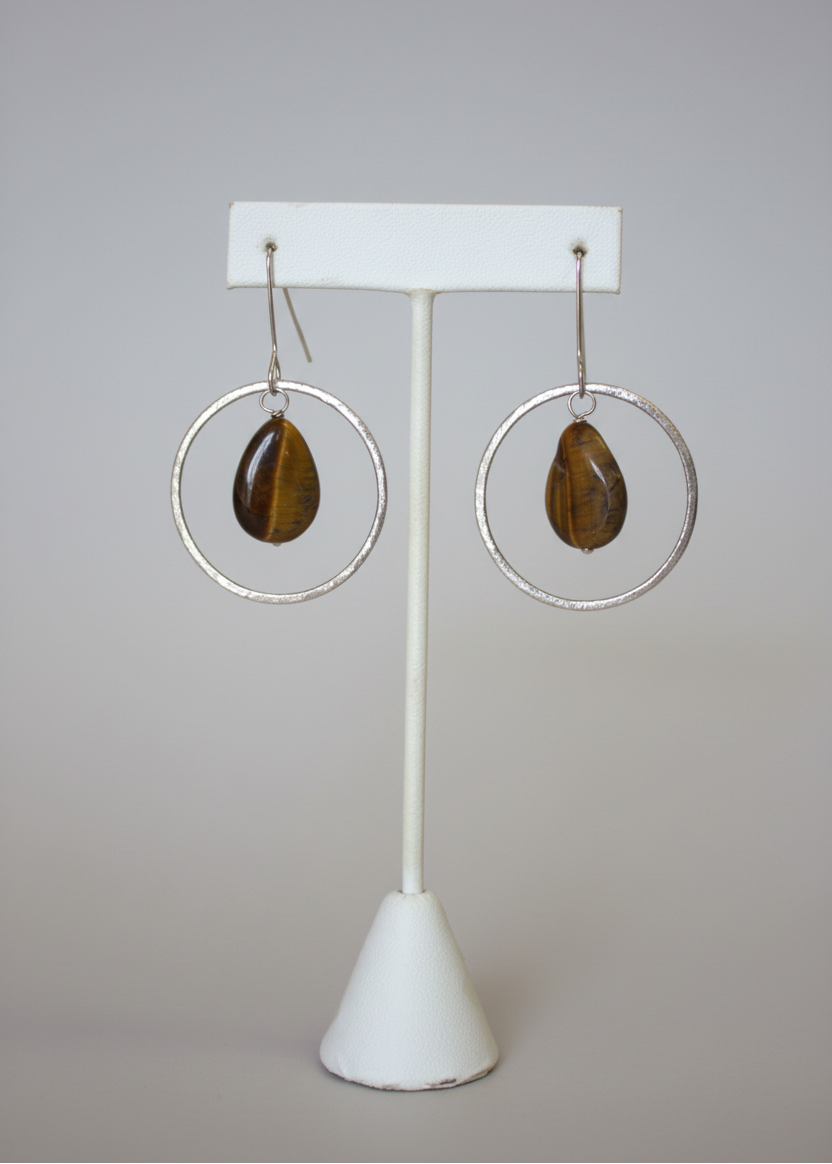 Pair of hoop earrings with brown stones on a white stand against a plain background