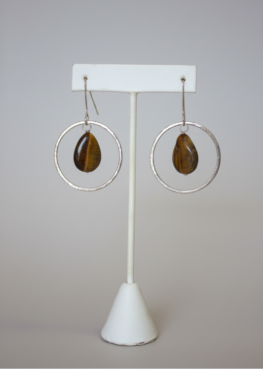 Pair of hoop earrings with brown stones on a white stand against a plain background