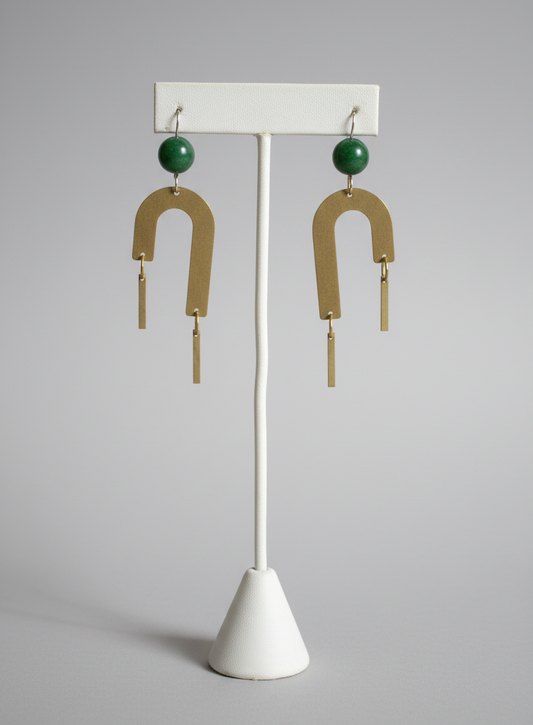 Gold earrings with green beads on a white stand against a bright background