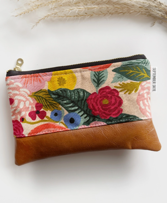Floral patterned pouch with brown leather bottom on a white background