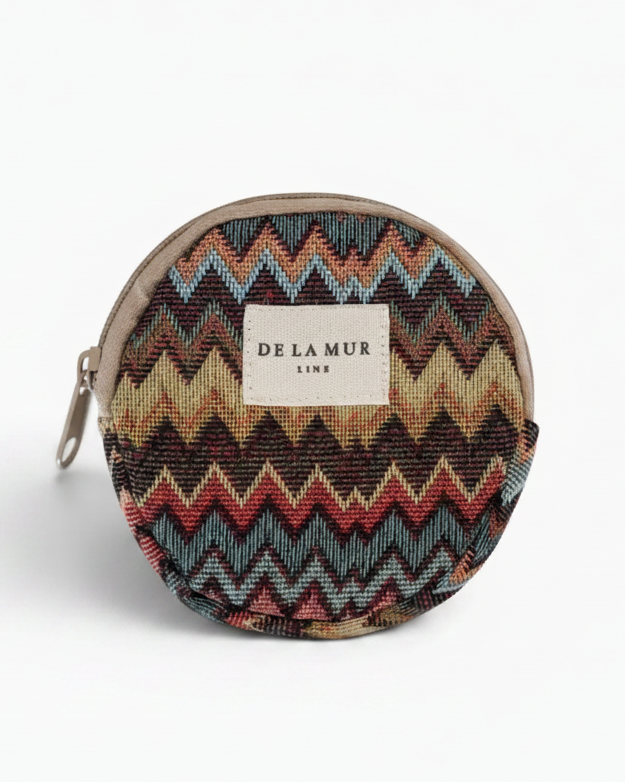 A round zippered pouch featuring a colorful chevron pattern in shades of blue, red, beige, and brown, with a beige fabric label reading 'DE LA MUR LINE' on the front.