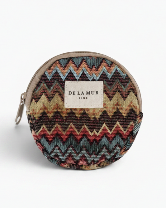 A round zippered pouch featuring a colorful chevron pattern in shades of blue, red, beige, and brown, with a beige fabric label reading 'DE LA MUR LINE' on the front.