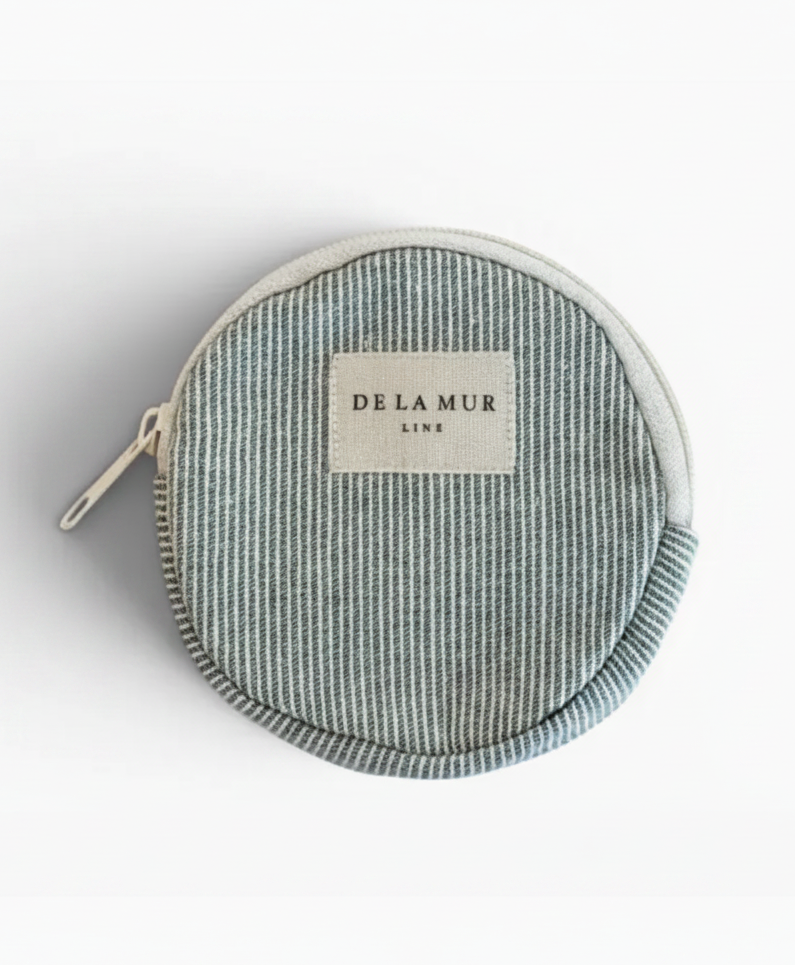 A round zippered pouch by Delamur Line featuring a vertical striped pattern in light blue and white, with a cream-colored brand label on the front.