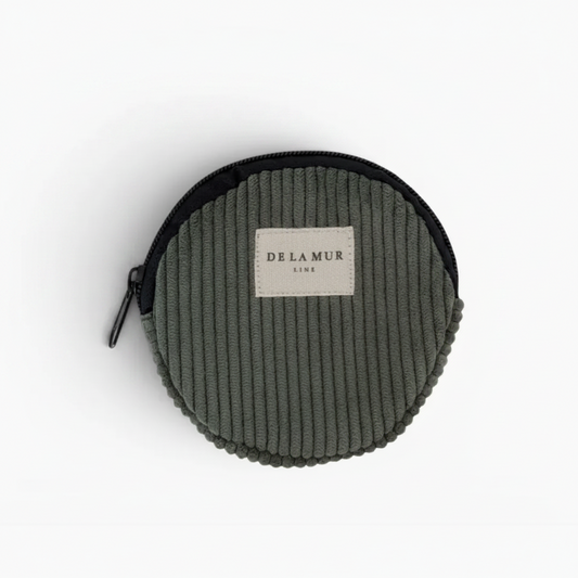 A round corduroy coin pouch in olive green with a black zipper and a beige brand label reading 'DE LA MUR LINE'.