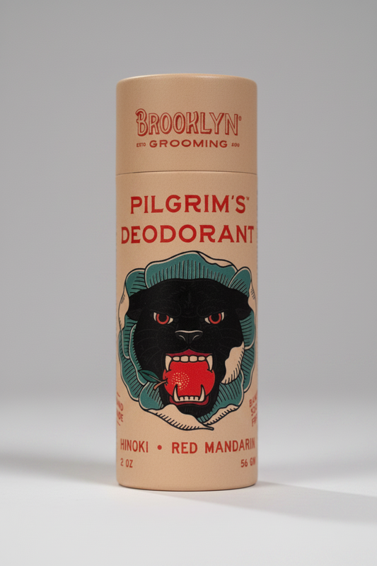 Brooklyn Grooming Pilgrim's Deodorant in a cylindrical cardboard container with a tan background, red text, and a black panther illustration with a red mandarin and green hat.