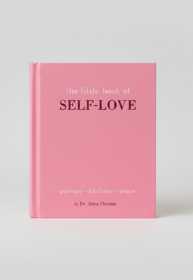 A pink hardcover book titled 'the little book of SELF-LOVE' with the words 'patience • kindness • peace' printed on the cover, styled on a light pink textured surface with decorative props.
