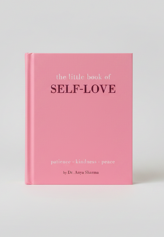 A pink hardcover book titled 'the little book of SELF-LOVE' with the words 'patience • kindness • peace' printed on the cover, styled on a light pink textured surface with decorative props.