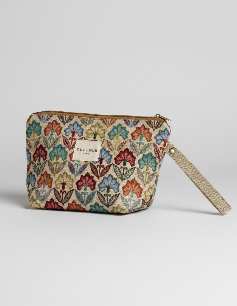 A cosmetic pouch featuring a colorful floral tapestry pattern on a cream background, with a beige wristlet strap and a gold zipper.