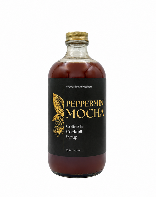 A bottle of Wood Stove Kitchen Peppermint Mocha Coffee & Cocktail Syrup, featuring a black label with gold lettering and a gold cap, set against a plain white background.