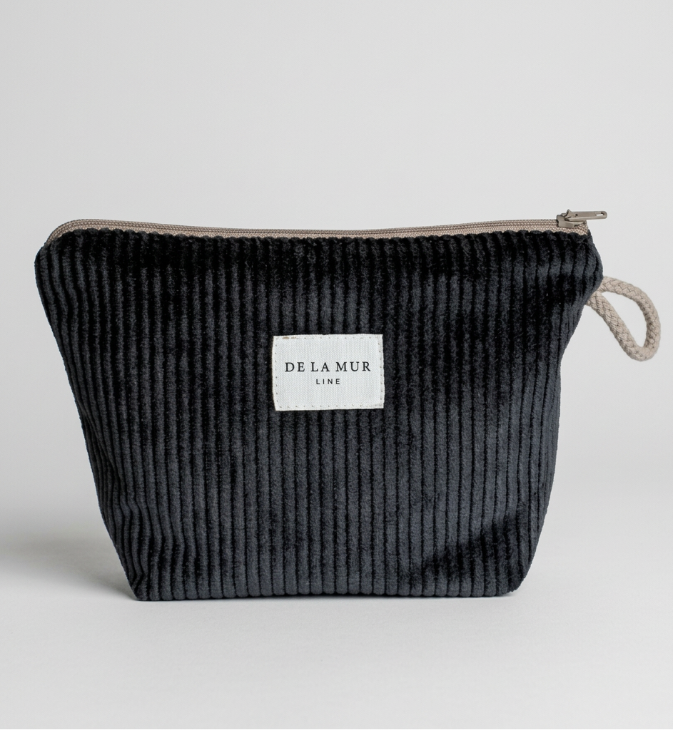 A black corduroy zippered pouch with a white rectangular label reading 'DELAMUR LINE' and a light gray fabric loop handle, shown on a plain white background.