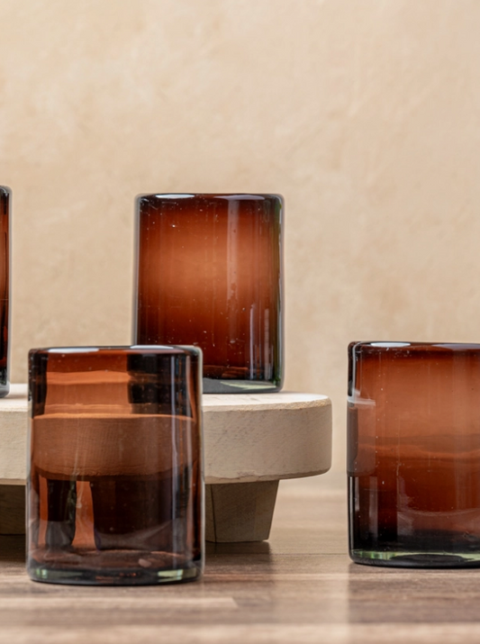 Set of brown glass candle holders on a wooden surface with a beige wall background