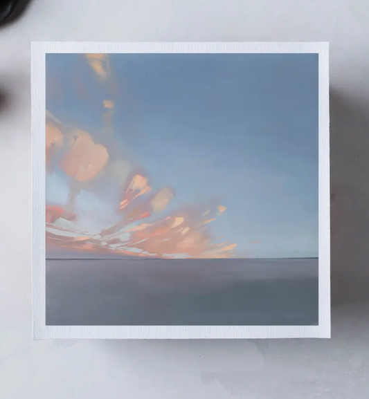 Framed photograph of a sunset or sunrise with a blue sky and fiery orange hues.