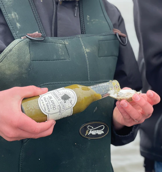 Person holding a bottle of olive oil with a label, wearing a green apron.