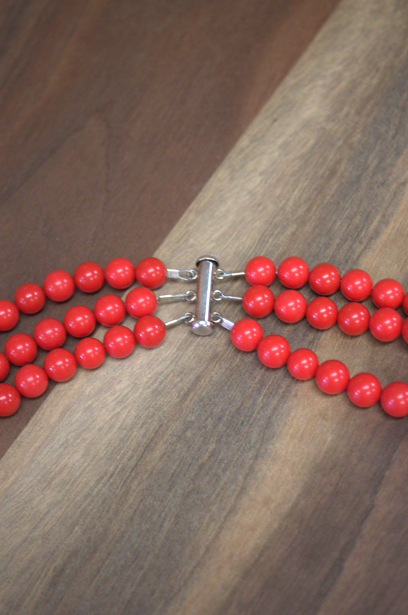 Red beaded necklace with a silver clasp on a wooden surface