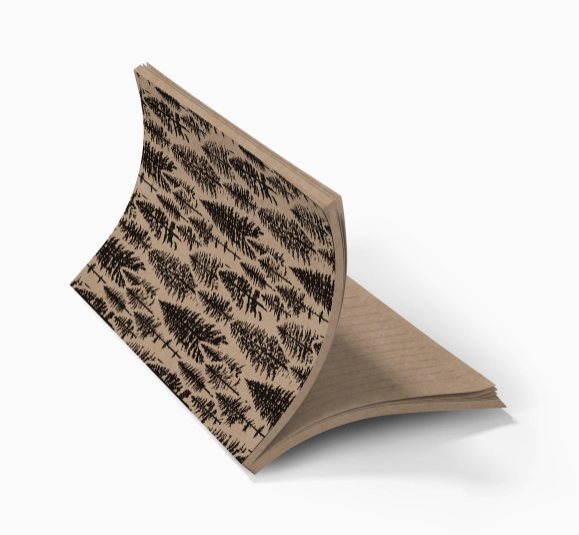 A single notebook or journal shown open at an angle on a plain white background. The cover has a repeating black pine tree pattern on a warm tan/beige base, and the interior pages are also tan with faint horizontal lines.