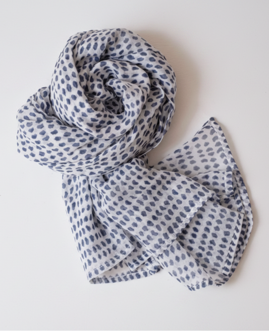A lightweight white scarf with a repeating blue watercolor-style dot pattern, styled in a loose spiral on a white background.
